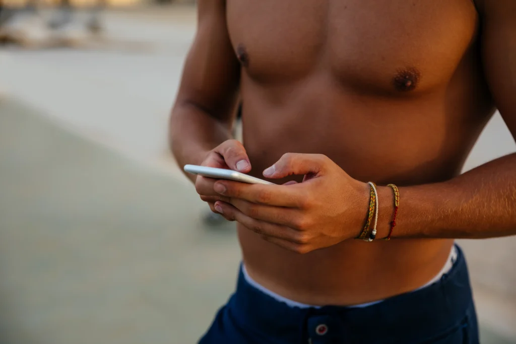 Hombre joven sin camiseta usando un teléfono móvil y escribiendo mensajes