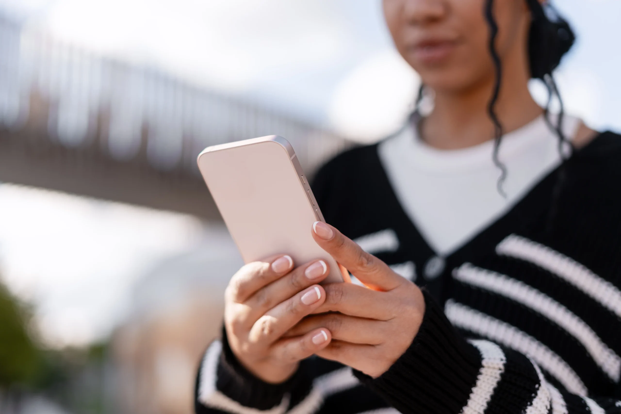 Mujer sosteniendo su teléfono móvil al aire libre, revisando notificaciones o conversaciones online.